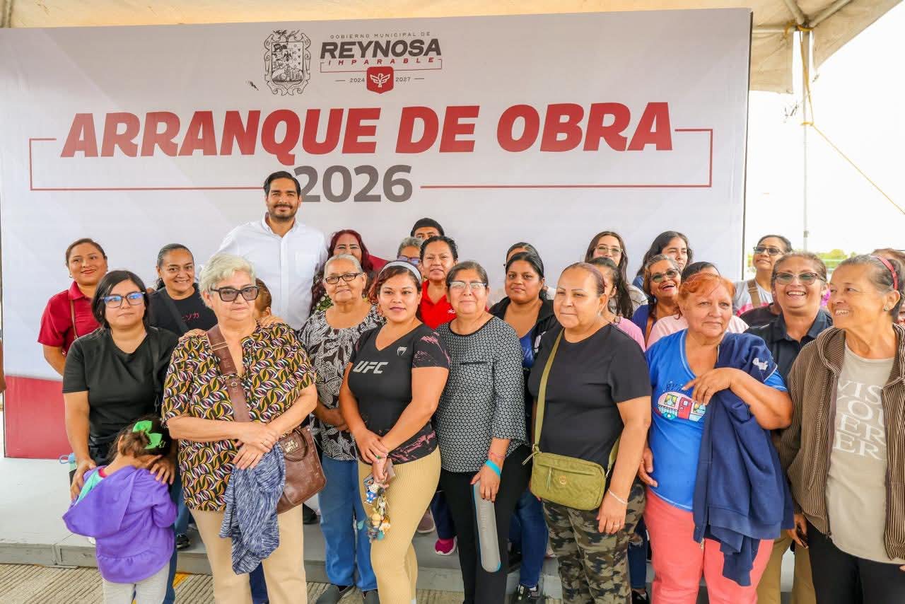A group of women poses for a photo at an event, with a banner in the background reading "ARRANQUE DE OBRA 2026."